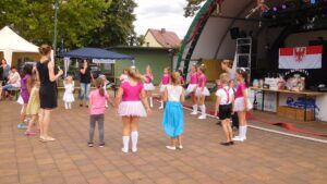 Kinder in rosa und weißen Kostümen tanzen auf einer Bühne