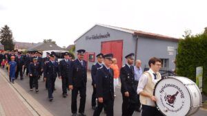 Eine Gruppe von Männern in Uniformen marschiert entlang einer Straße. Ein Mann schlägt auf eine große Trommel.