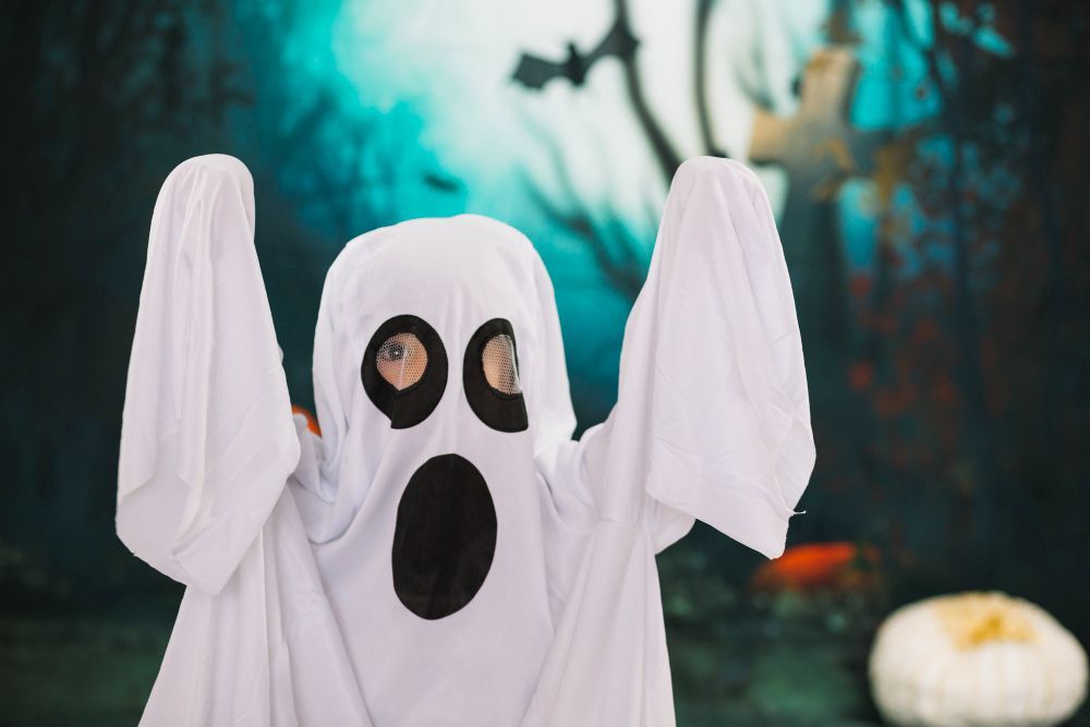 Ein Kind ist als Geist verkleidet und hat einen überraschten Gesichtsausdruck. Der Hintergrund ist dunkel und unheimlich.