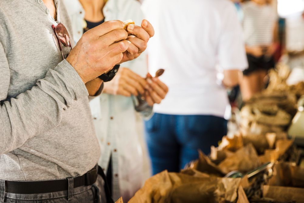 Ein Mann probiert ein Lebensmittel auf einem Markt. Im Hintergrund stehen andere Personen.