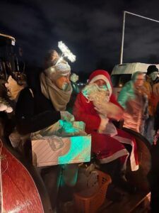 Sankt Nikolaus sitzt auf einem Wagen und hält ein Geschenk.