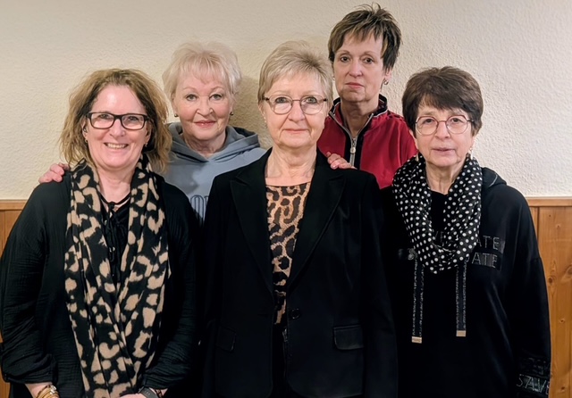 Ein Foto von fünf Damen, die zusammen stehen und lächeln. Sie tragen verschiedene Outfits und Accessoires.